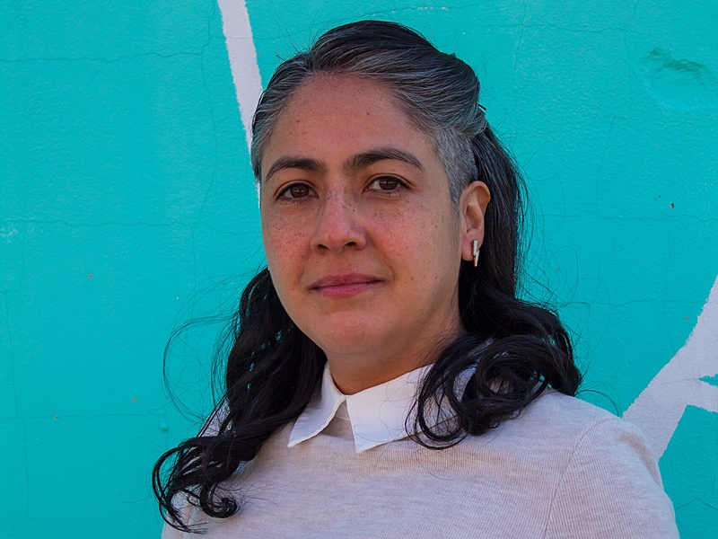 Maria Celleri stands in front of a wall that is painted light blue