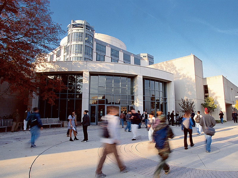 Blurred photo of people walking outside of the Albin O. Kuhn Library at UMBC.