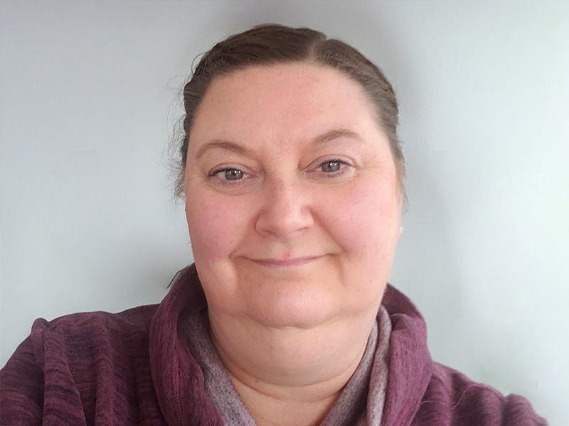 Human with hair pulled back wearing a purple jacket.