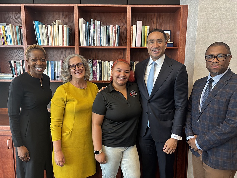 Five people are posed, smiling in front of a bookcase.