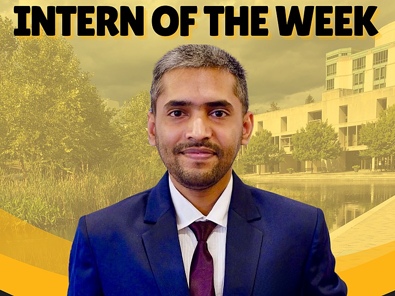 Professional headshot of a man smiling in a blue suit with maroon tie.