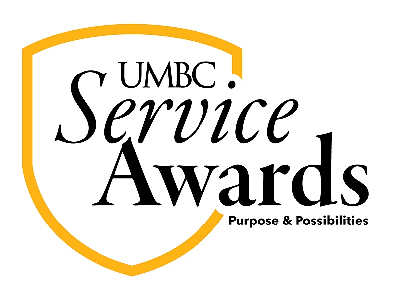 UMBC Service Awards logo with a gold shield outline. The text inside the shield is black and says "UMBC Service Awards" in a mix of serif and script-like fonts. Below "Service Awards" are the words "Purpose & Possibilities.
