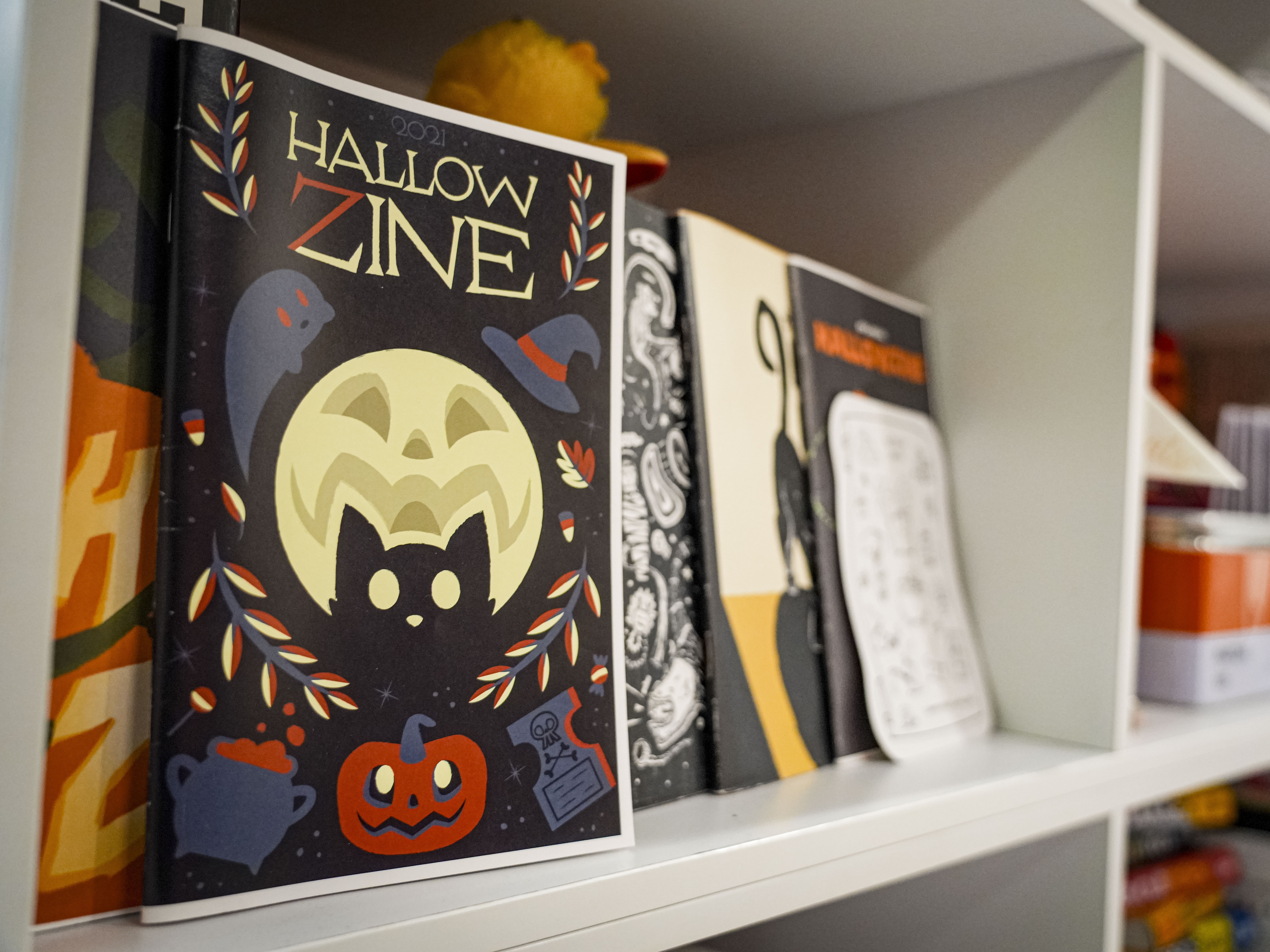 2021 Hallowzine on display along with previous years on a bookshelf