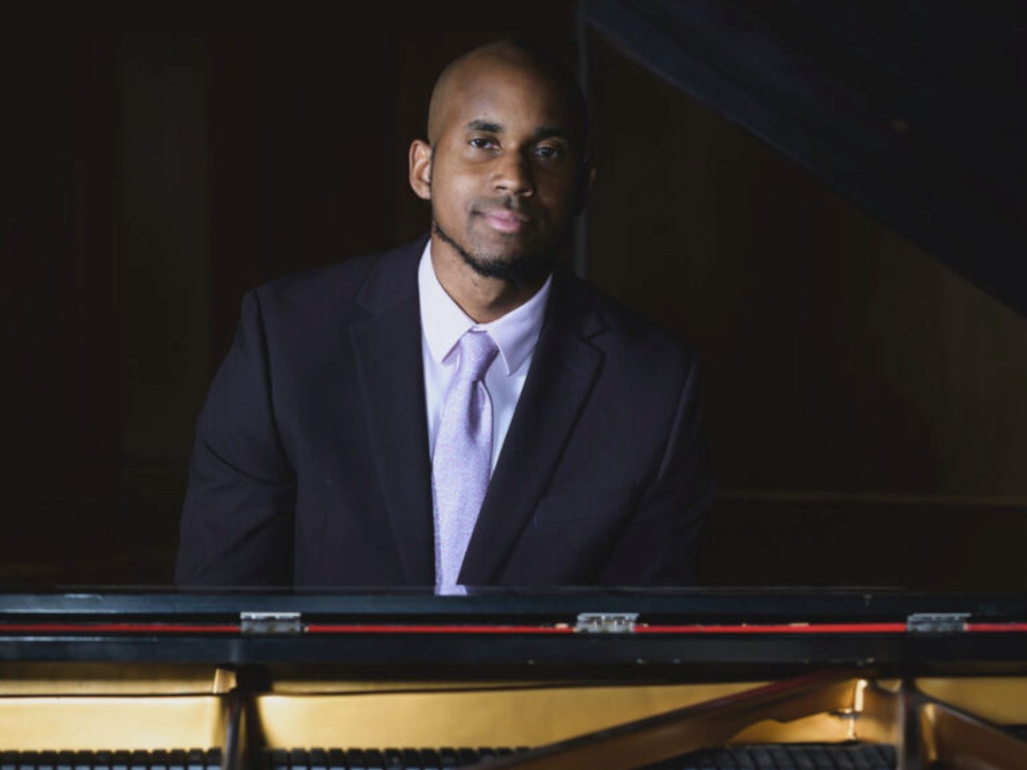 A man in a suit sits behind a piano.
