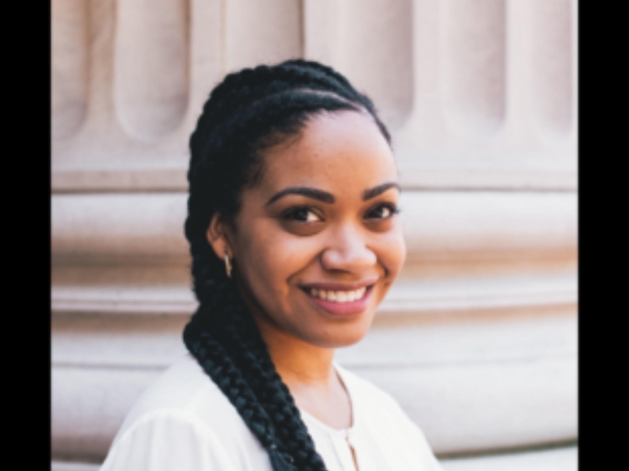 headshot of smiling woman with long, dark braids in a white blouse.