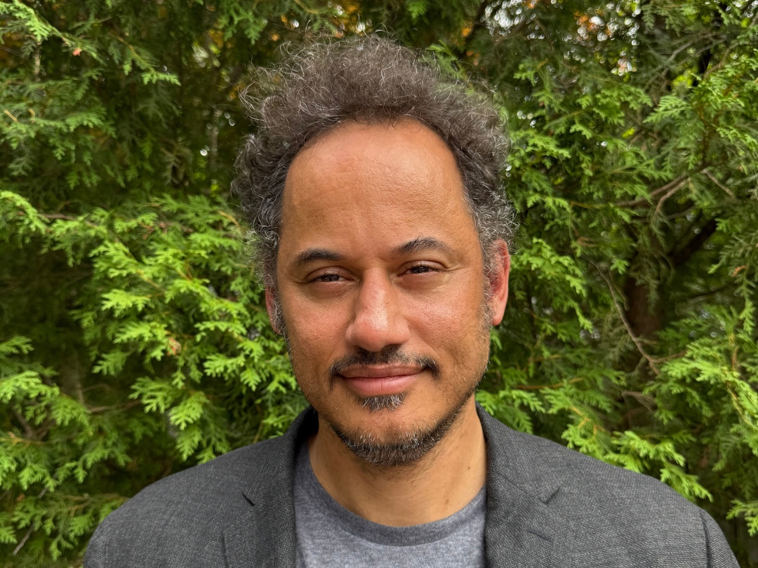 Daniel Steinmetz-Jenkins is smiling towards the camera. He is standing outside in front of trees.
