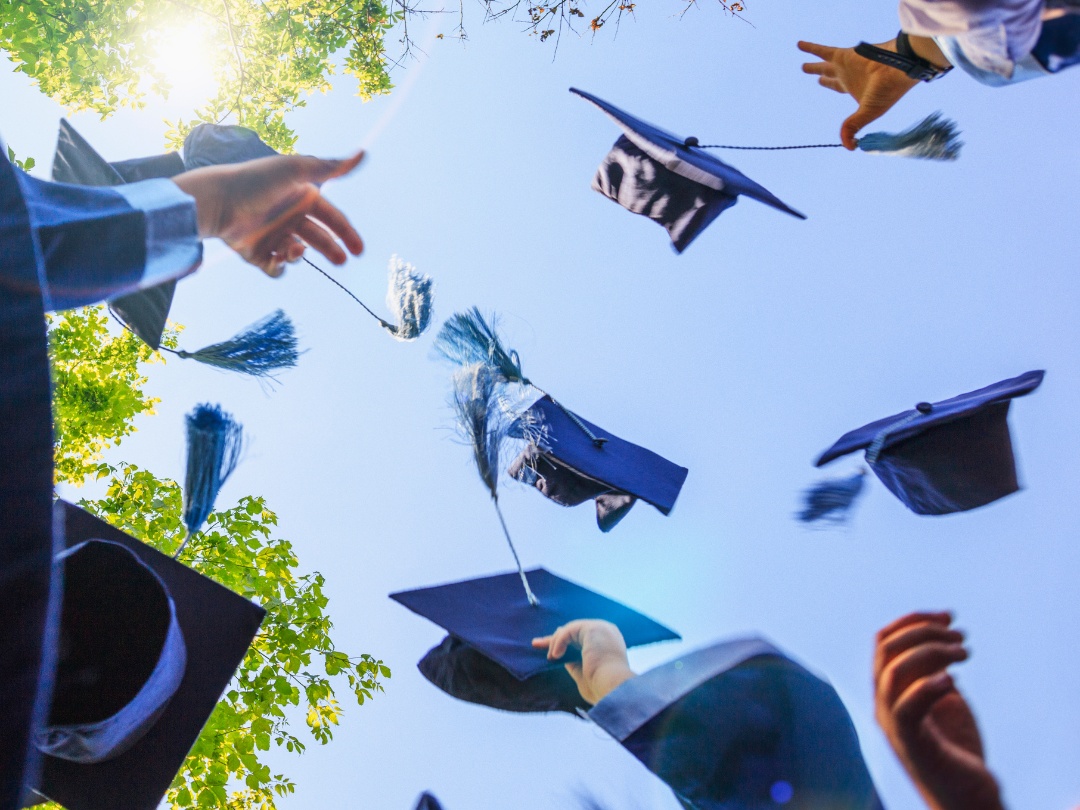 A photo looking up towards the sky with graduation caps in the that students threw up in the air.