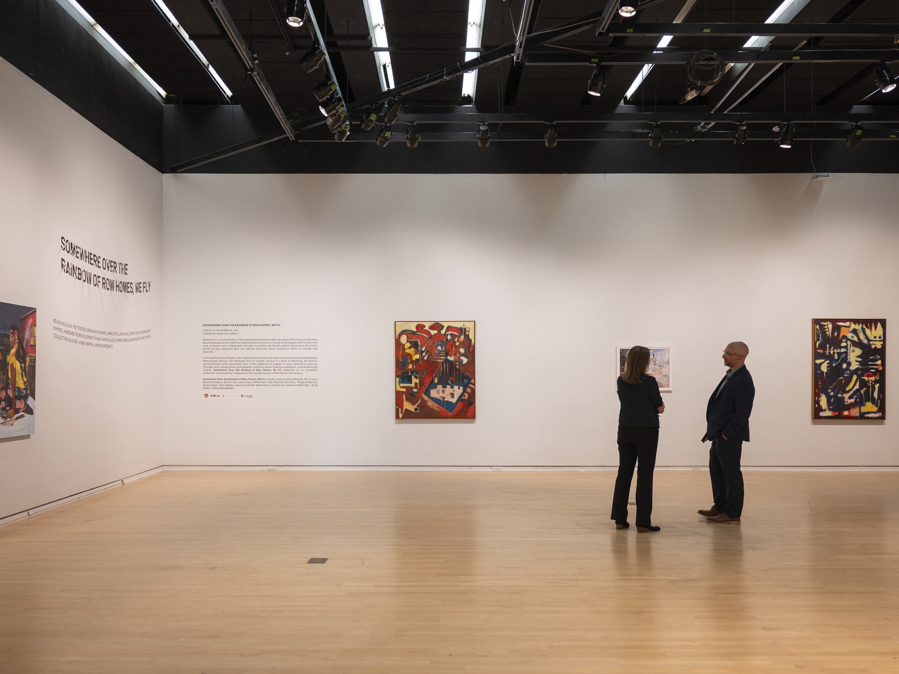 Two people stand in an art gallery looking at artworks hung on white walls.