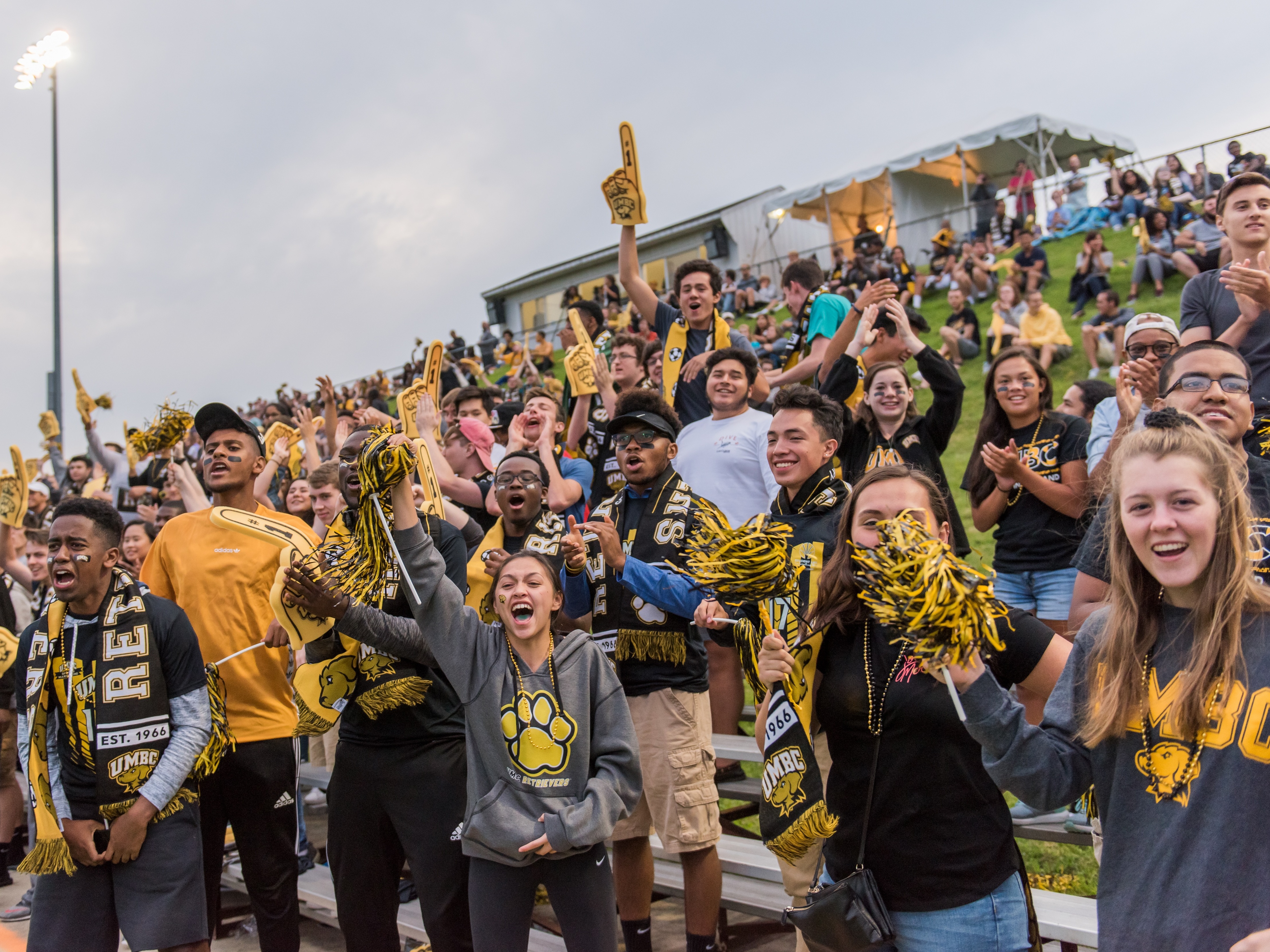 UMBC students dressed in UMBC gear cheering outside at a soccer game.