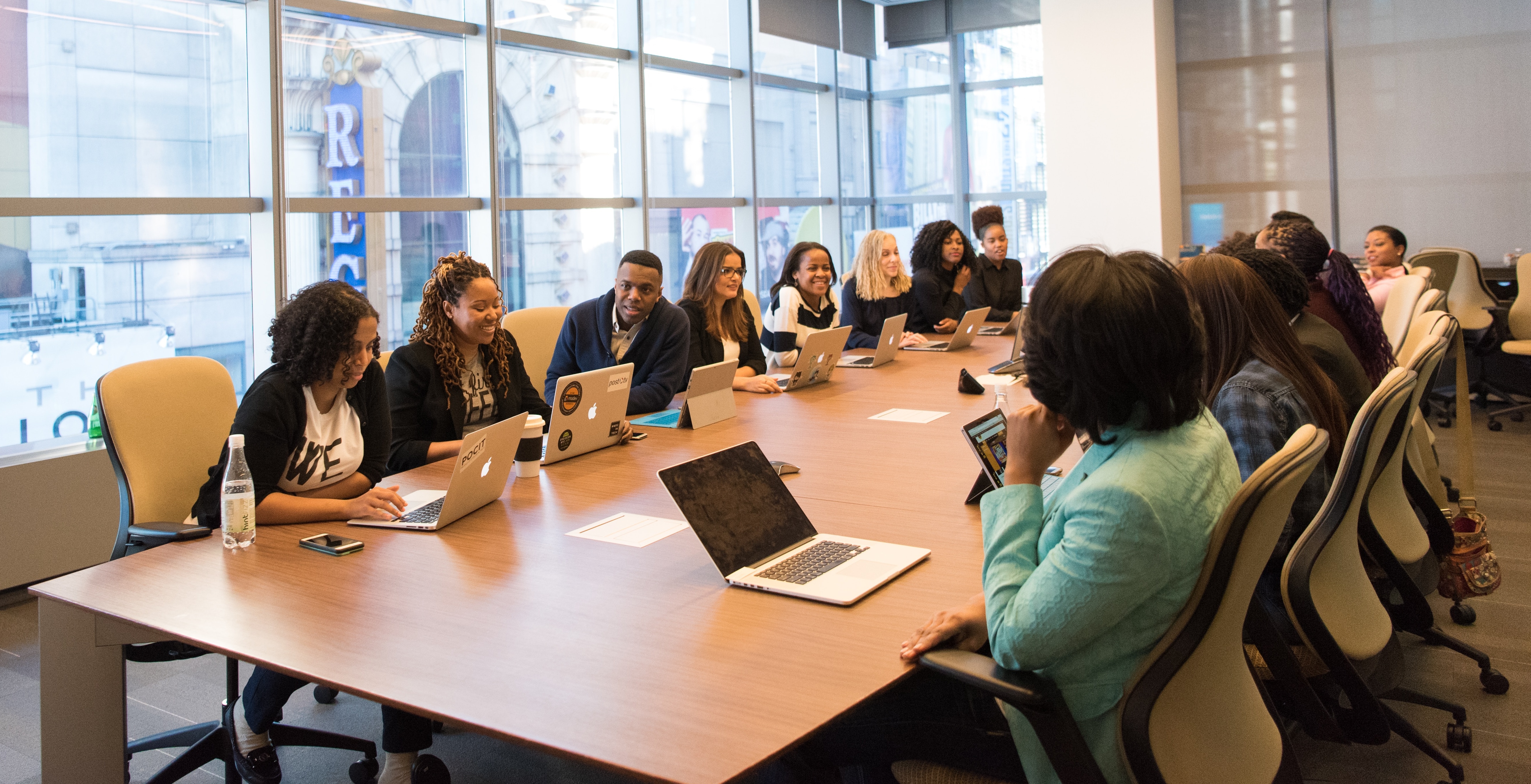 a diverse group of professionals with laptops seated around a large rectangular table